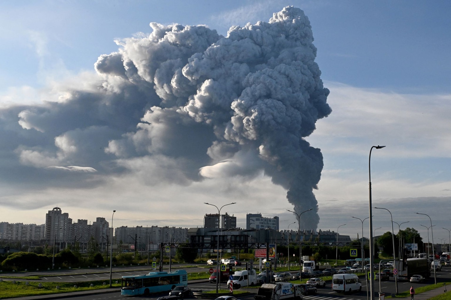 Cars drive along the road as smoke rises above residential buildings from a warehouse for a Russian e-commerce giant near Saint Petersburg after being hit by Ukrainian drones early on July 24, 2026 (AFP via Getty Images)