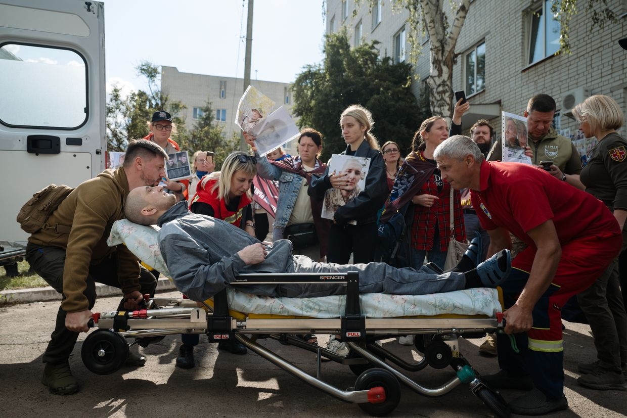 Medics load a seriously wounded soldier, recently released from Russian captivity, into an ambulance as relatives of prisoners of war hold portraits of their loved ones in northern Ukraine, on June 12, 2025. 