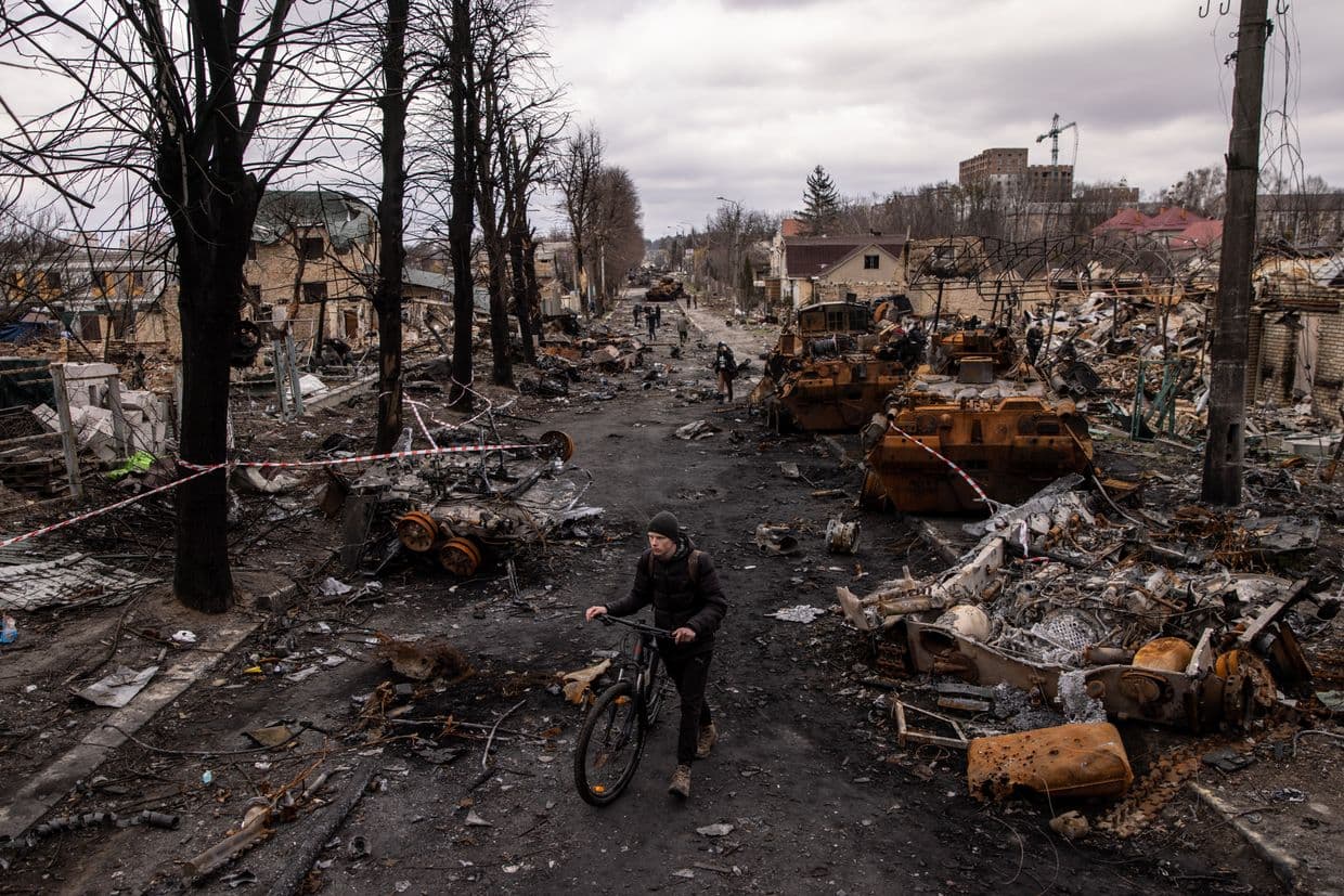A man pushes his bike through debris and destroyed Russian military vehicles