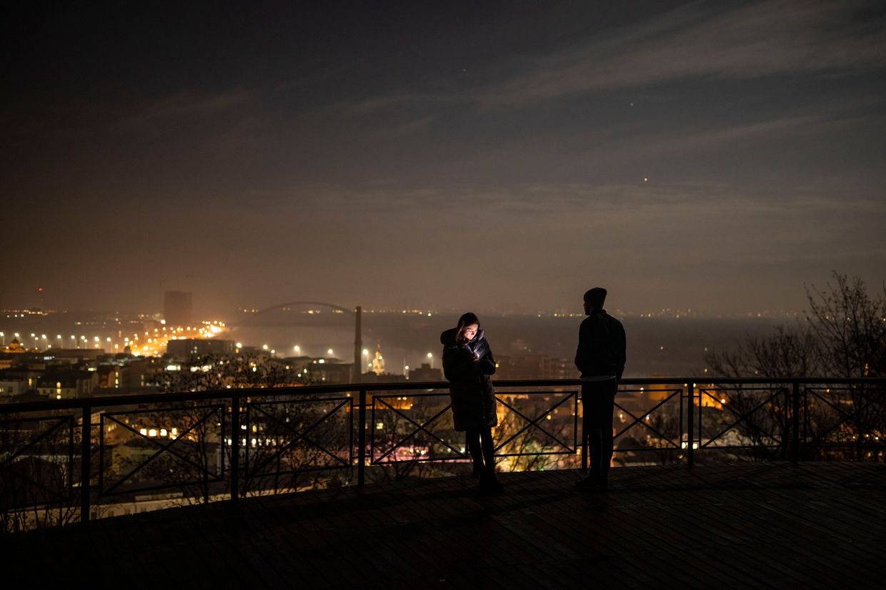 A man looks out over Kyiv as a woman checks her phone during a local power outage in Kyiv, Ukraine, on Nov. 8, 2022.