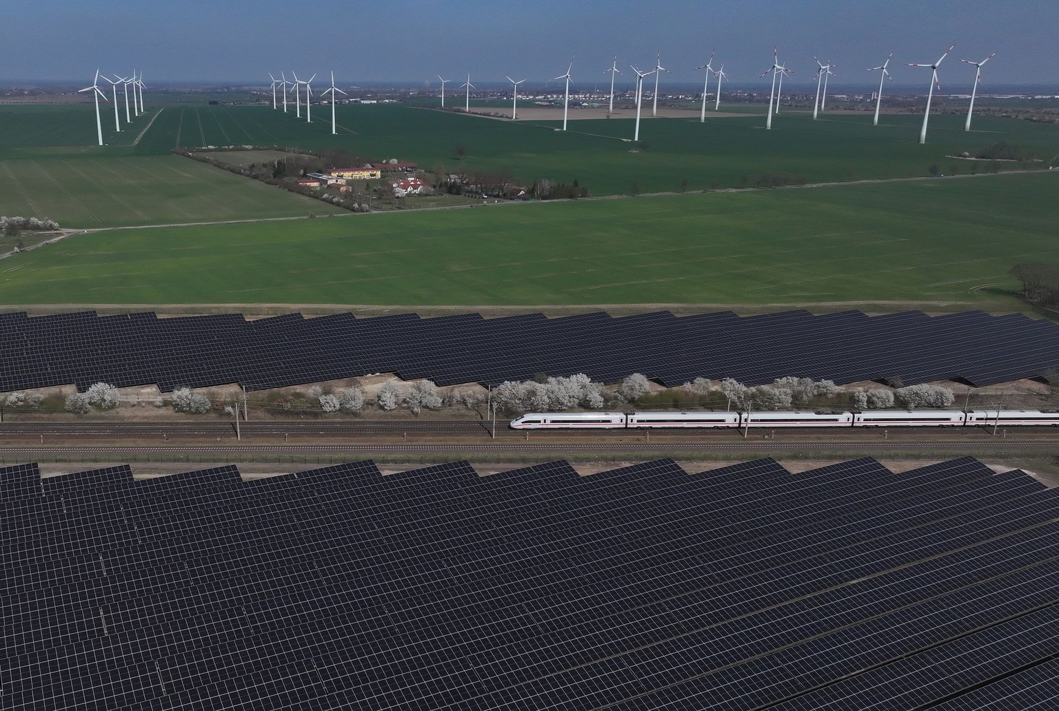 A high-speed Intercity Express train of German state railways Deutsche Bahn passes a solar energy park and wind turbines near Nauen, Germany, on April 2, 2025.