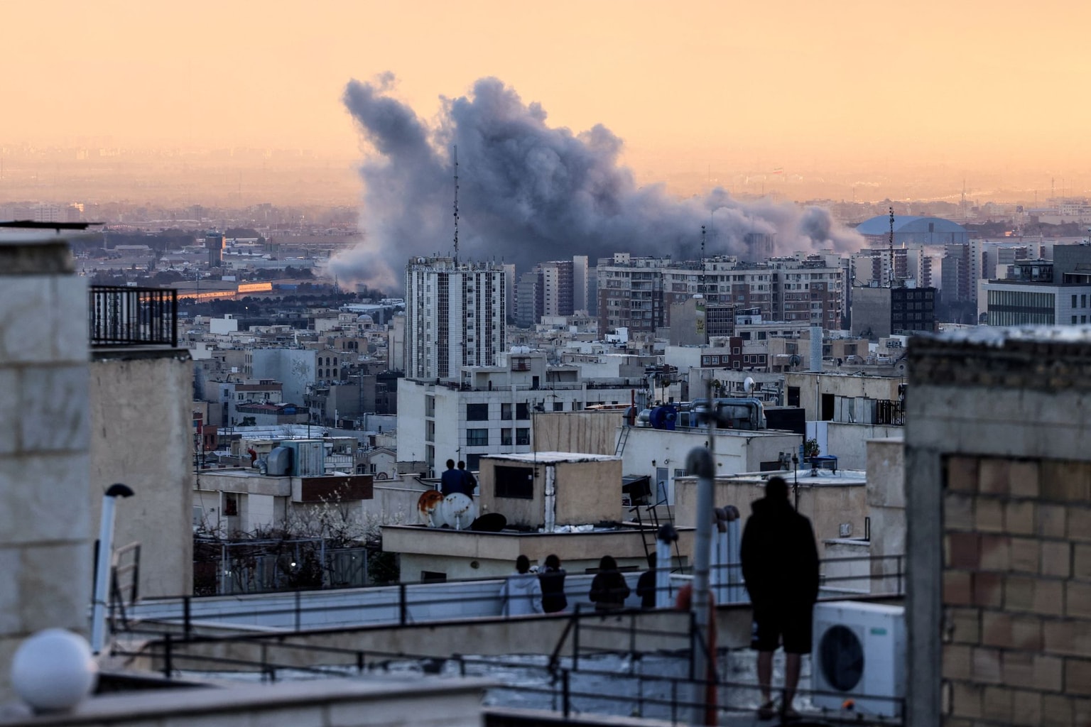 A person stands on a roof looking at a plume of smoke following a strike in Tehran, Iran, on March 3, 2026.