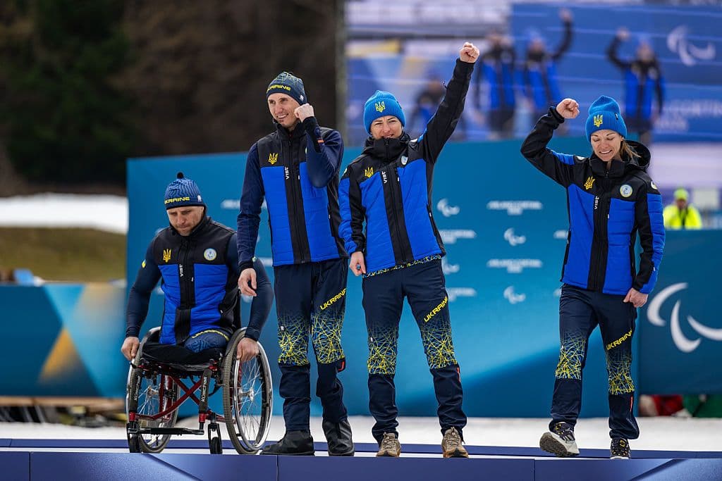 Four Ukrainian paralympic athletes in blue and yellow sports gear cheer