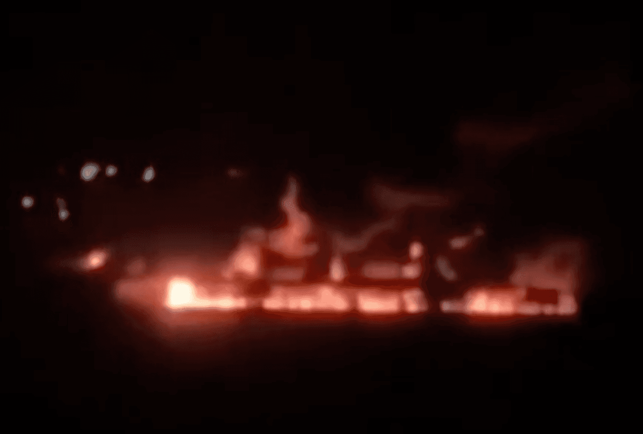 A fire burns at an industrial city under a black sky