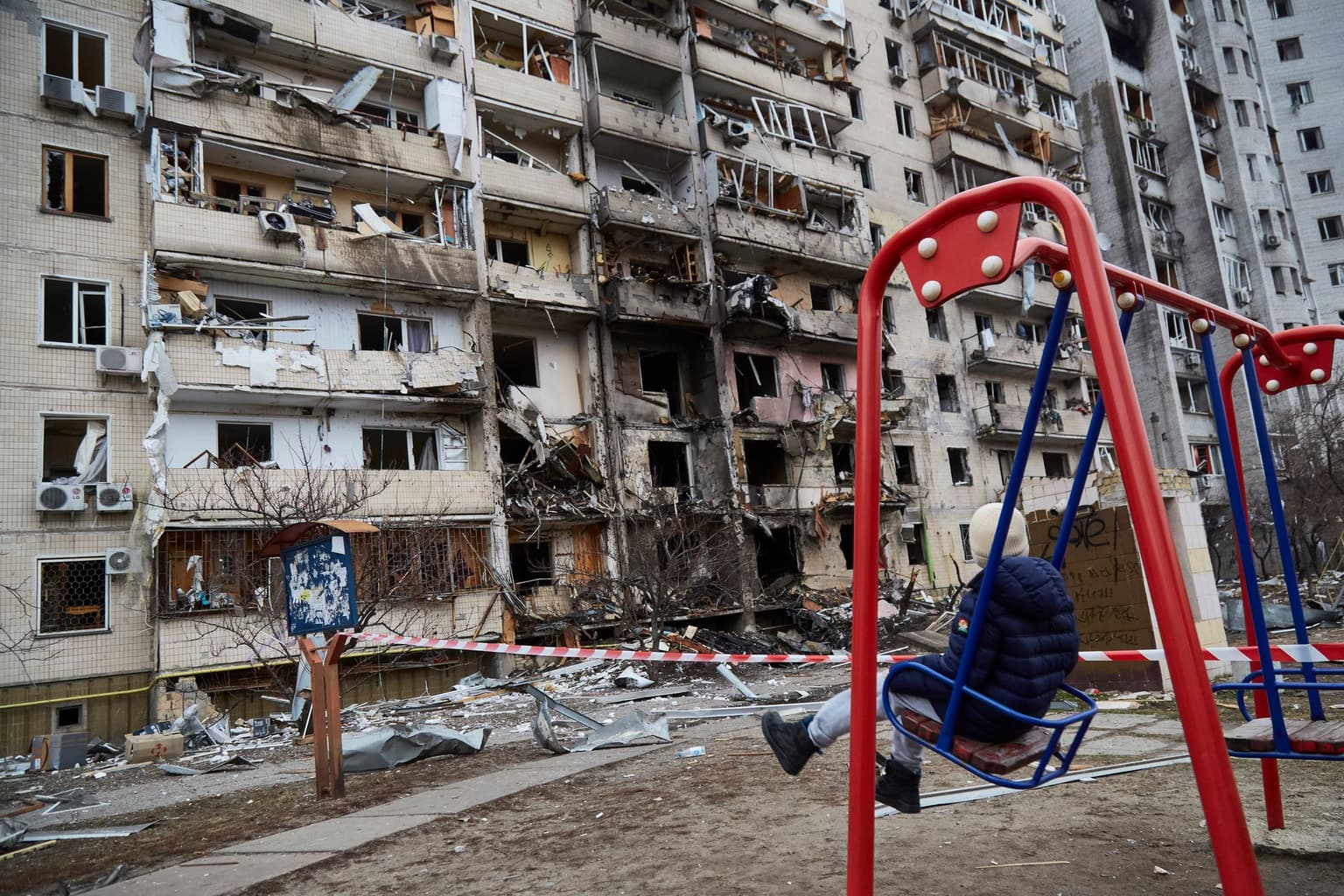 A child sits on a swing in front of a residential building damaged by a missile strike in Kyiv, Ukraine, on Feb. 25, 2022.