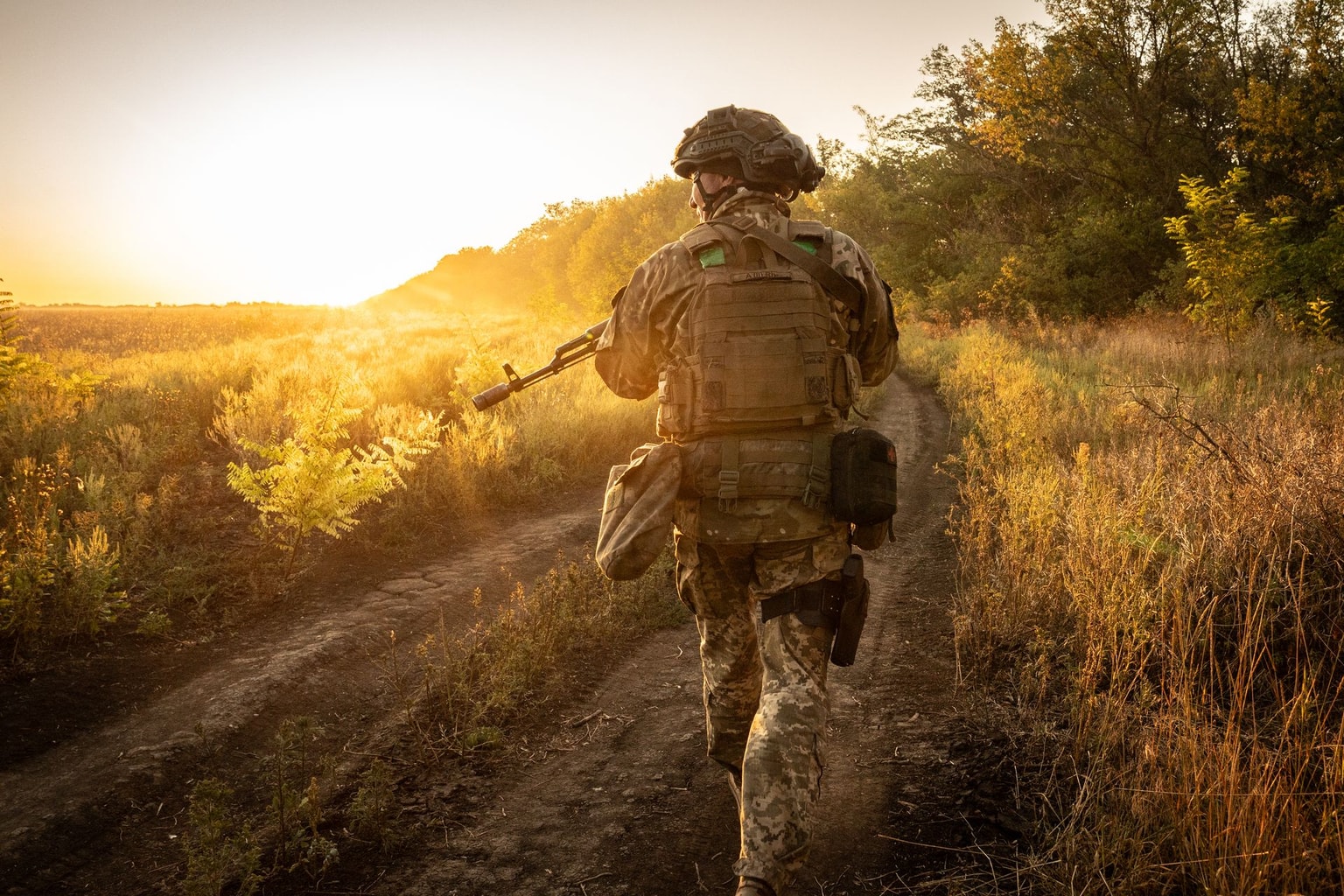 A Ukrainian soldier of the 148th Artillery Brigade walks along a dirt road at sunrise toward a position in Dnipropetrovsk Oblast, Ukraine, on Sept. 4, 2025. (Patryk Jaracz / The Kyiv Independent)