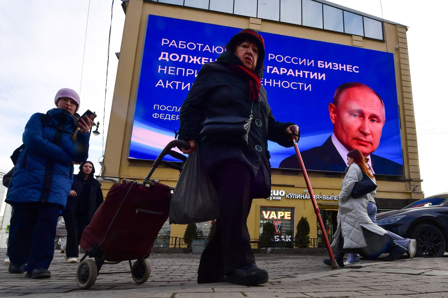 People pass by a digital screen displaying an image of Russian President Vladimir Putin in Saint Petersburg, Russia on March 13, 2024.