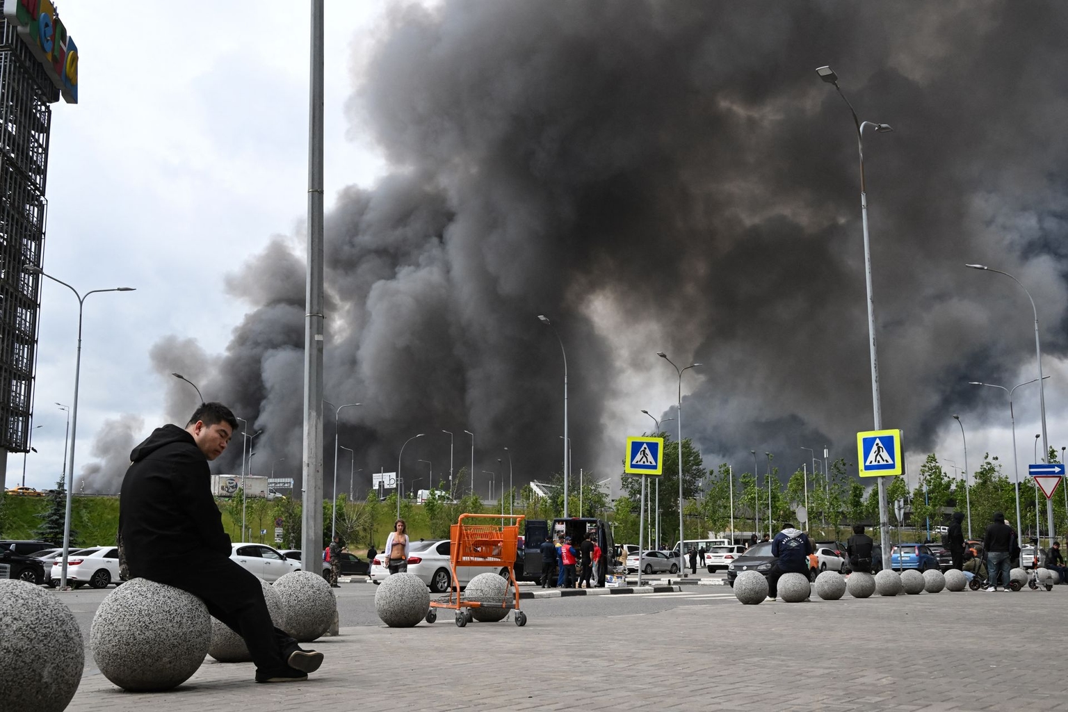People are seen outside a shopping mall as black smoke rises from the area of the Gazprom Neft oil refinery on the south-eastern outskirts of Moscow, Russia, on June 18, 2026