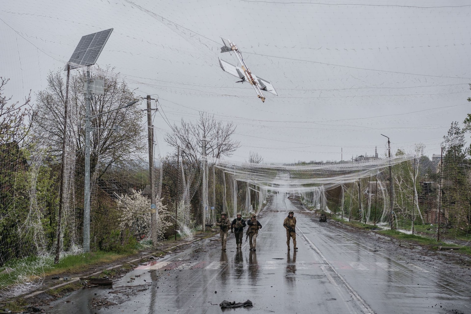 Members of the 24th Brigade of the Armed Forces of Ukraine walk along a road covered by anti-drone netting with a drone stuck in it while hunting Russian drones between Druzhkivka and Olexiivo-Druzhkivka, Donetsk Oblast, Ukraine, on April 24, 2026. (Serhii Korovayny/The Kyiv Independent)