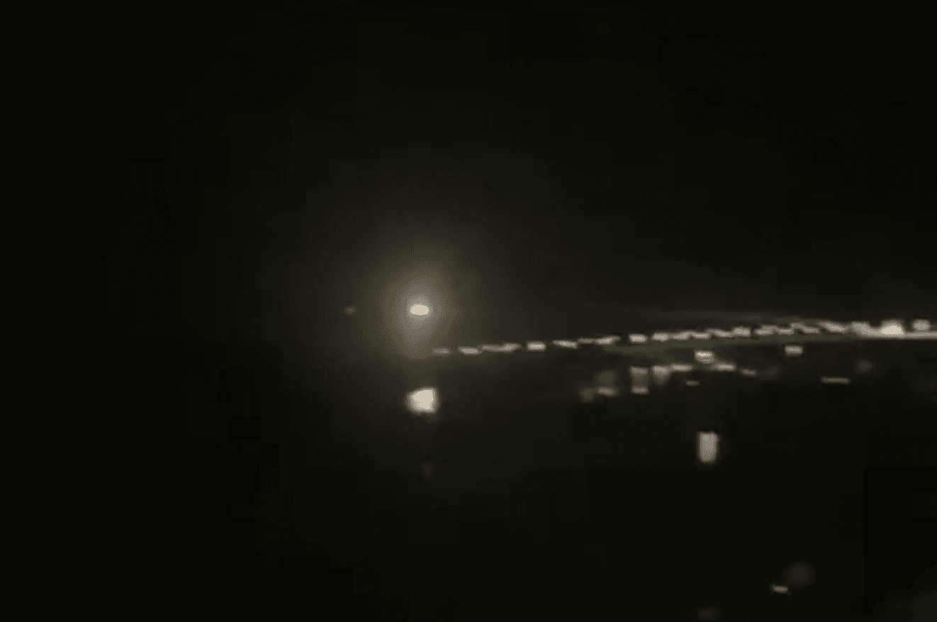 A bright spark flies over a cityscape under a night sky